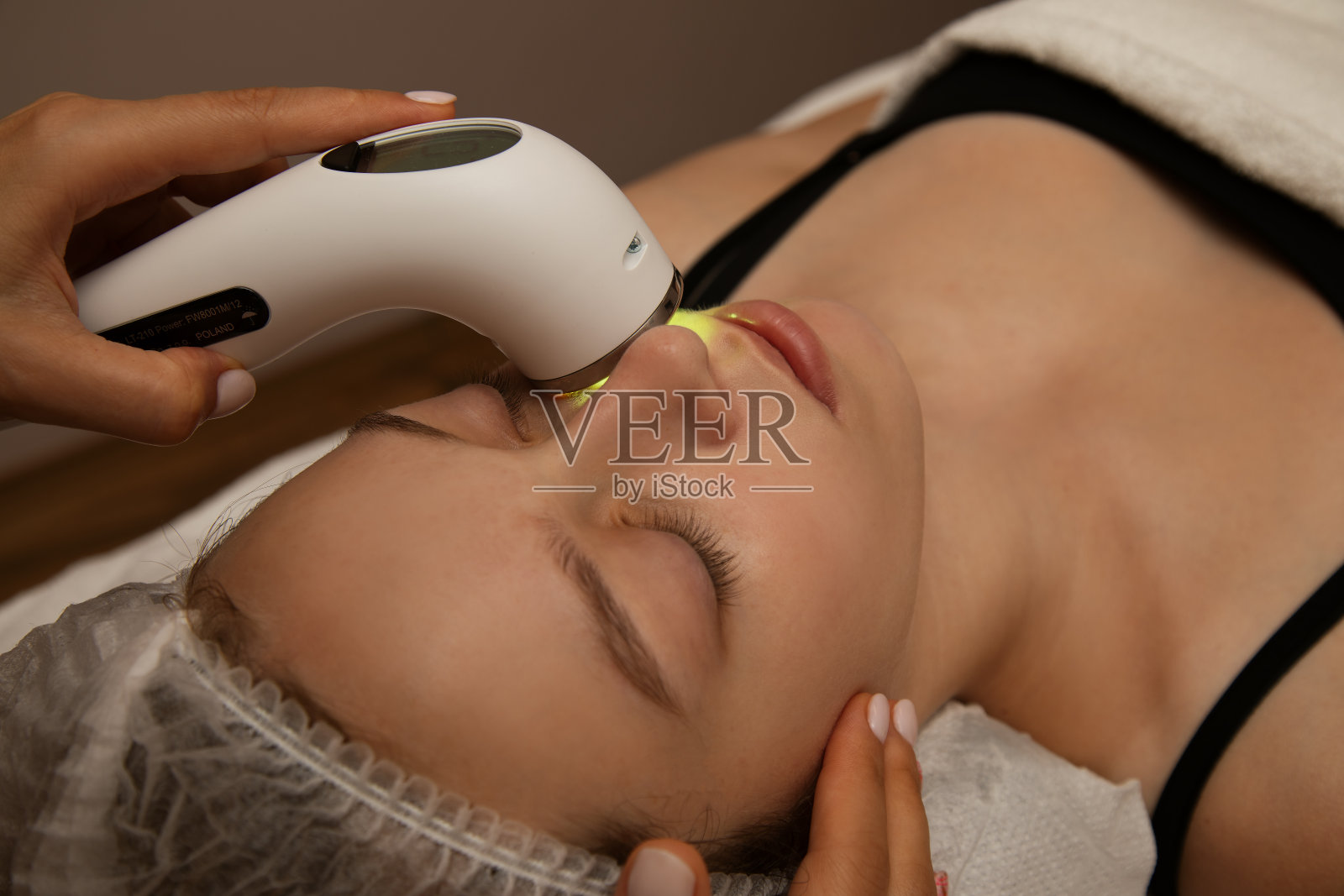年轻女性接受面部治疗与电穿孔美容装置，激光美容，抗痤疮护理，抗衰老程序照片摄影图片