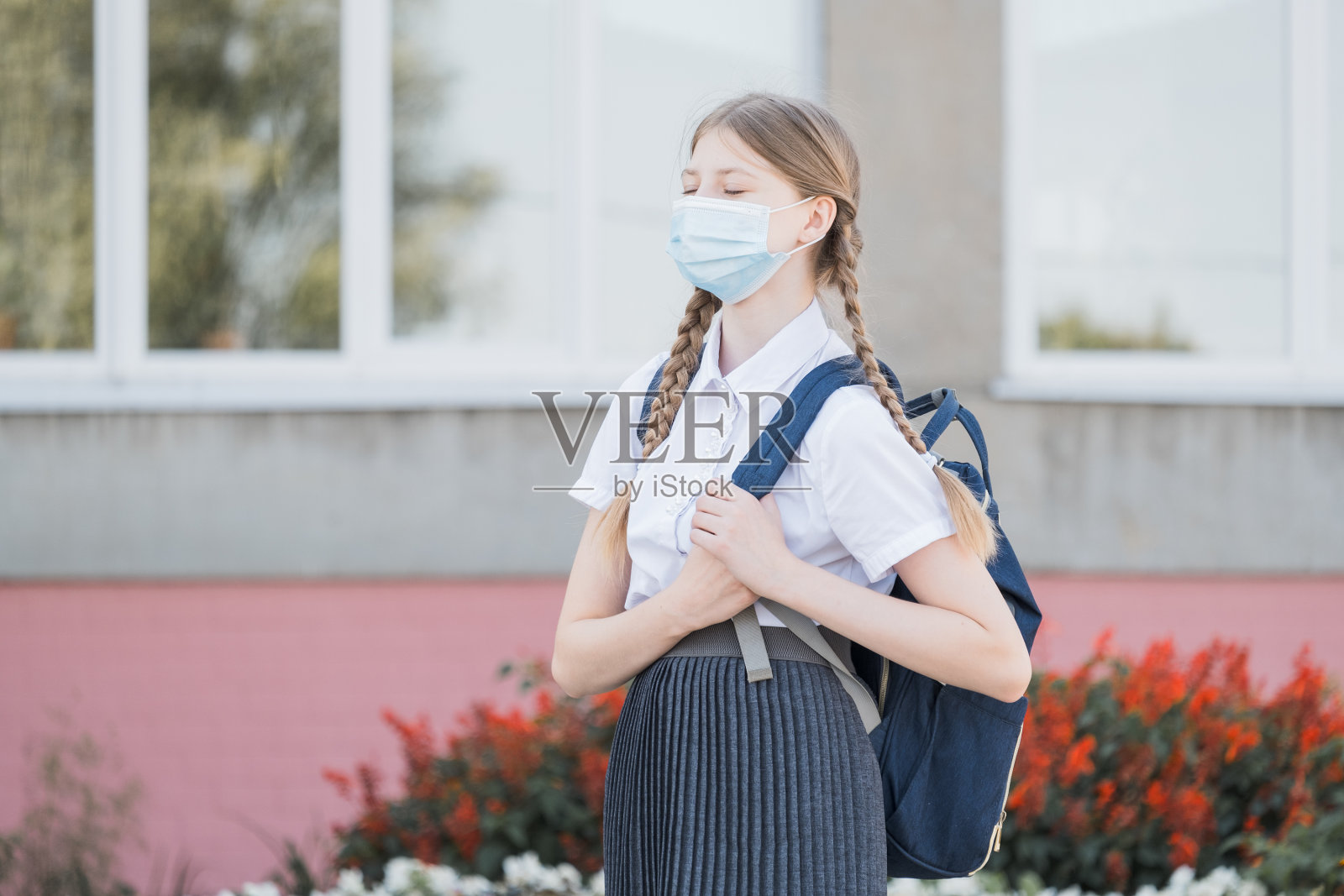 戴口罩的孩子在covid-19隔离和封锁后返回学校。回到学校，女大学生戴着防毒面具，背着背包、书和笔记本电脑走在校园里照片摄影图片