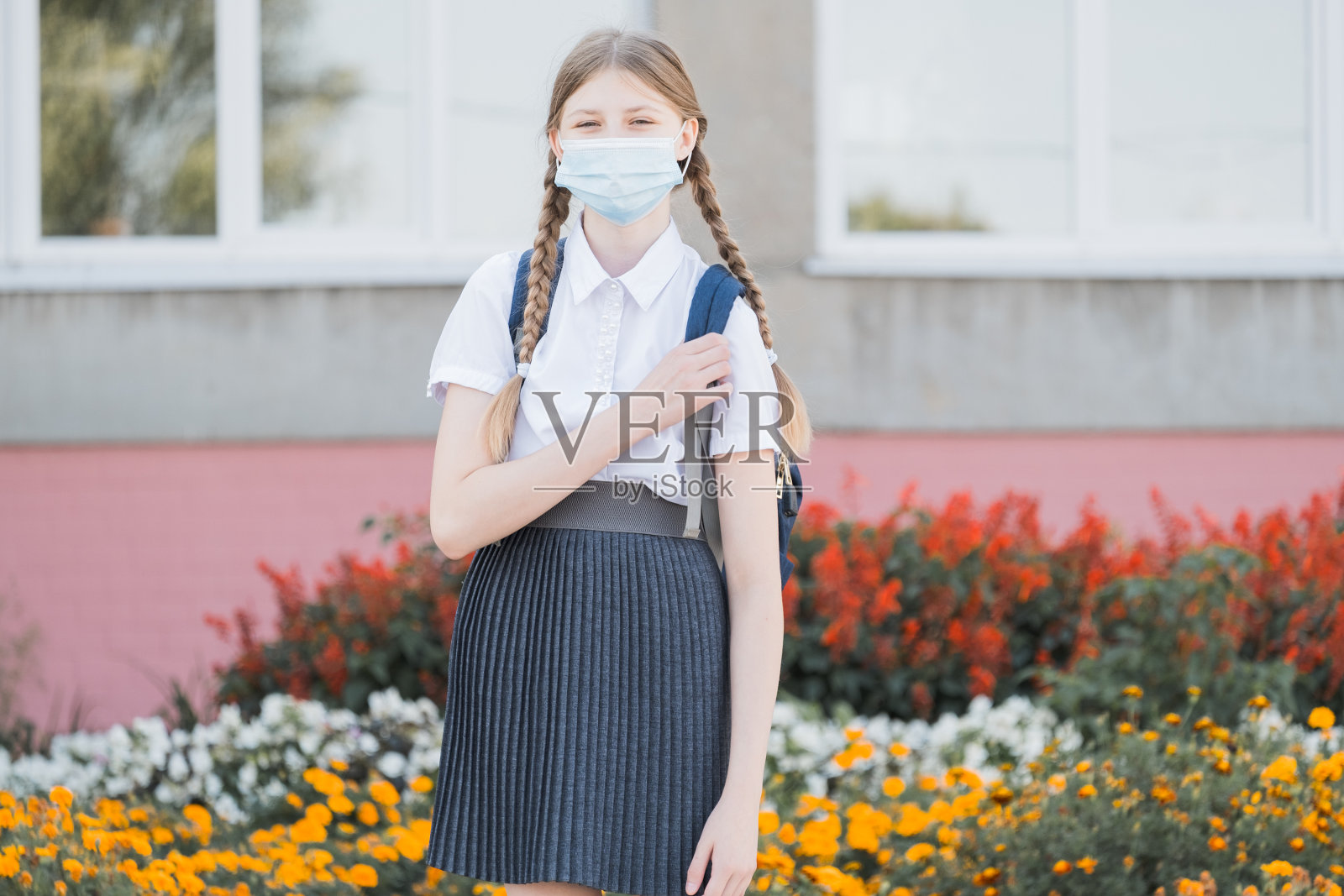 戴口罩的孩子在covid-19隔离和封锁后返回学校。回到学校，女大学生戴着防毒面具，背着背包、书和笔记本电脑走在校园里照片摄影图片