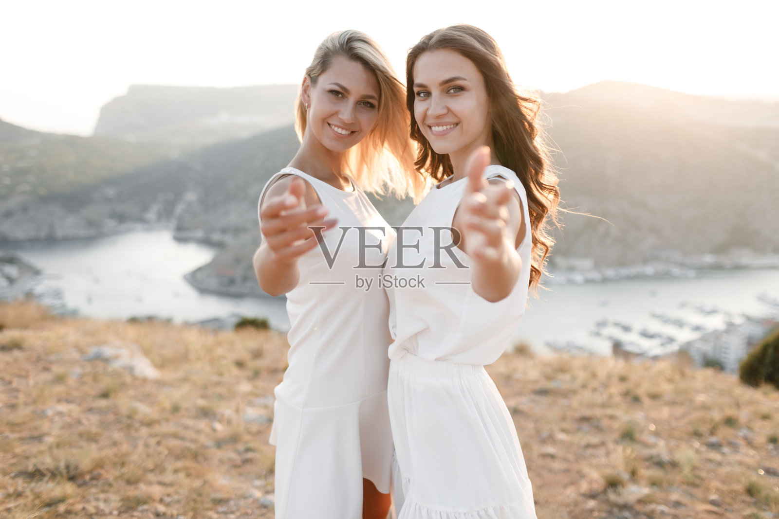 年轻的妇女戴着太阳帽，穿着白色的衣服在山顶上野餐，可以看到山脉和海湾照片摄影图片