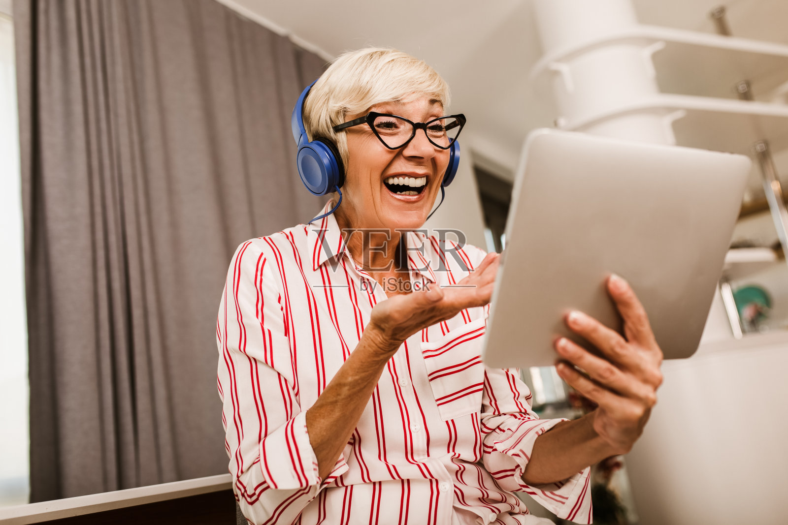 一个快乐的成熟女人一边向别人挥手，一边在家里用电子平板电脑进行视频通话。照片摄影图片