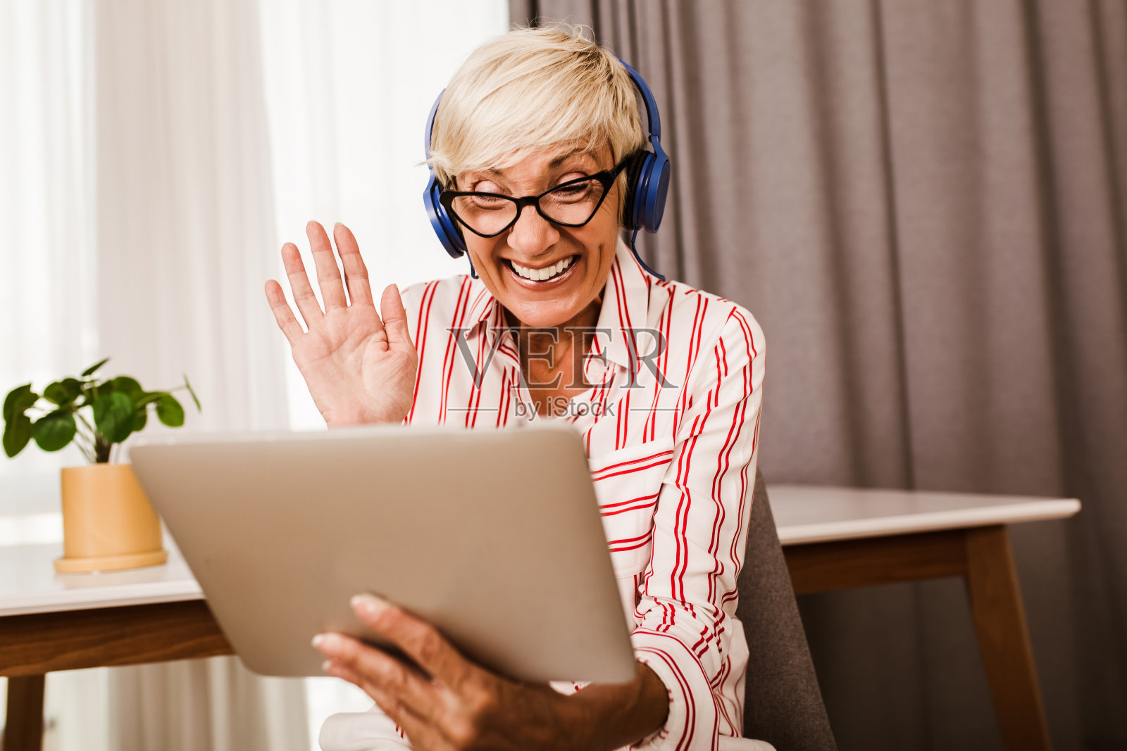 一个快乐的成熟女人一边向别人挥手，一边在家里用电子平板电脑进行视频通话。照片摄影图片