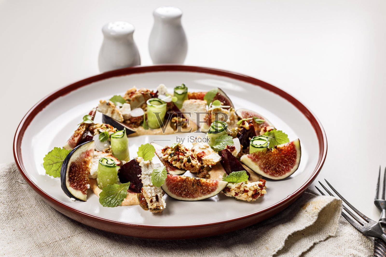 美味的夏季沙拉，配有成熟的无花果，山羊奶酪，新鲜的黄瓜卷，甜菜根，芥末叶和番茄酱。没有肉的夏季沙拉。美味健康的食物。照片摄影图片