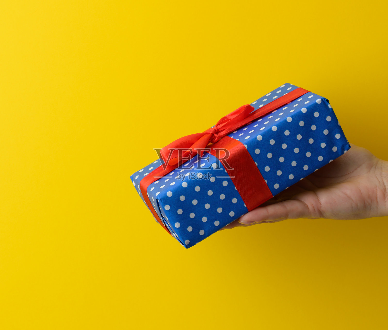 女性手拿着黄色背景上的蓝色礼品盒照片摄影图片