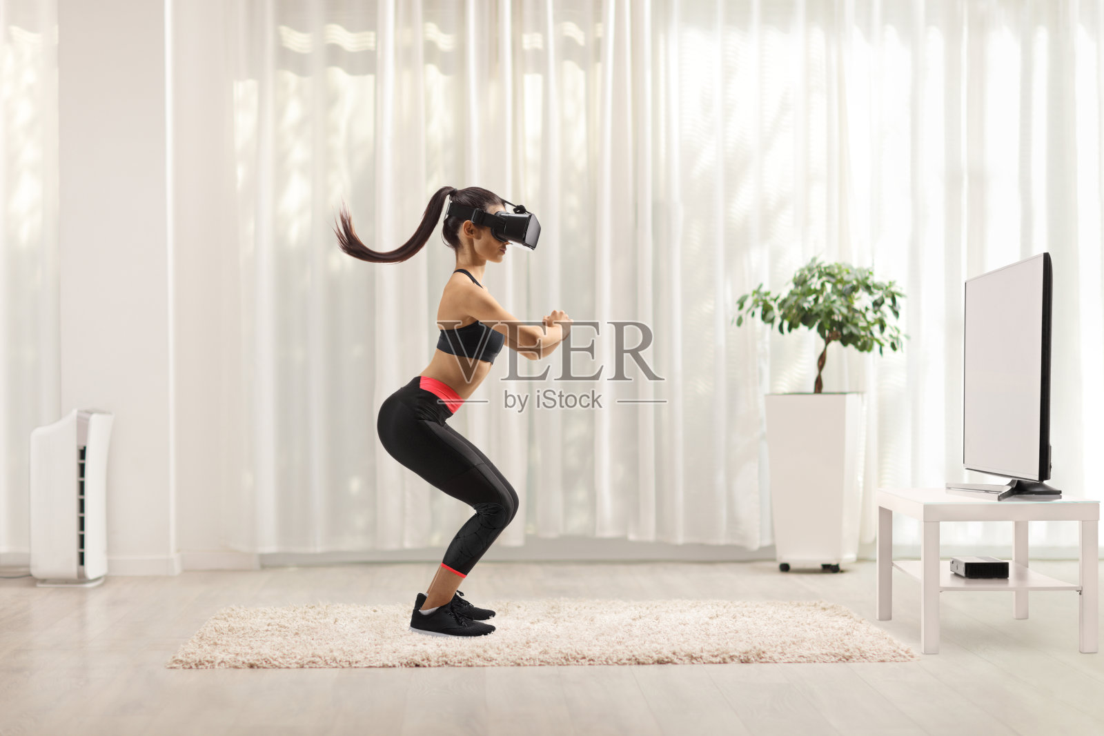 一个年轻的女人与vr头戴在电视机前锻炼的全长侧面镜头照片摄影图片