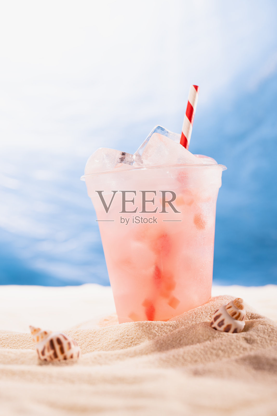 在热带海滩上，用塑料杯装冰的新鲜的粉红色鸡尾酒，复制空间，垂直。夏天在海滨度假和野餐。照片摄影图片