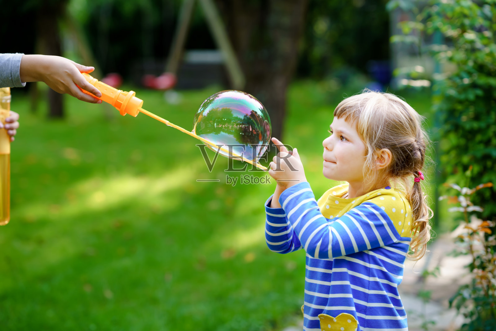快乐的金发学前班小女孩开心地吹肥皂泡鼓风机。可爱的孩子在阳光明媚的夏日玩耍。快乐、积极、有趣、健康的孩子。儿童活动。照片摄影图片