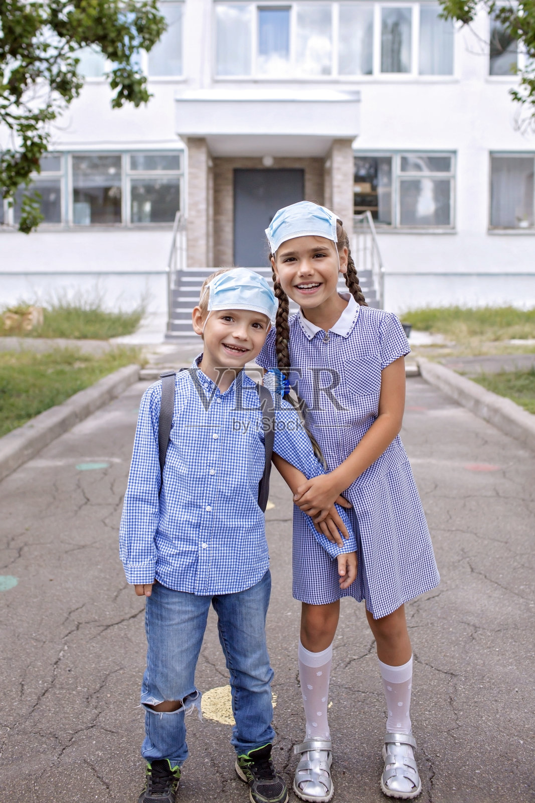 回到学校。戴着医用口罩的兄弟姐妹们在第一天不上班前待在门口照片摄影图片
