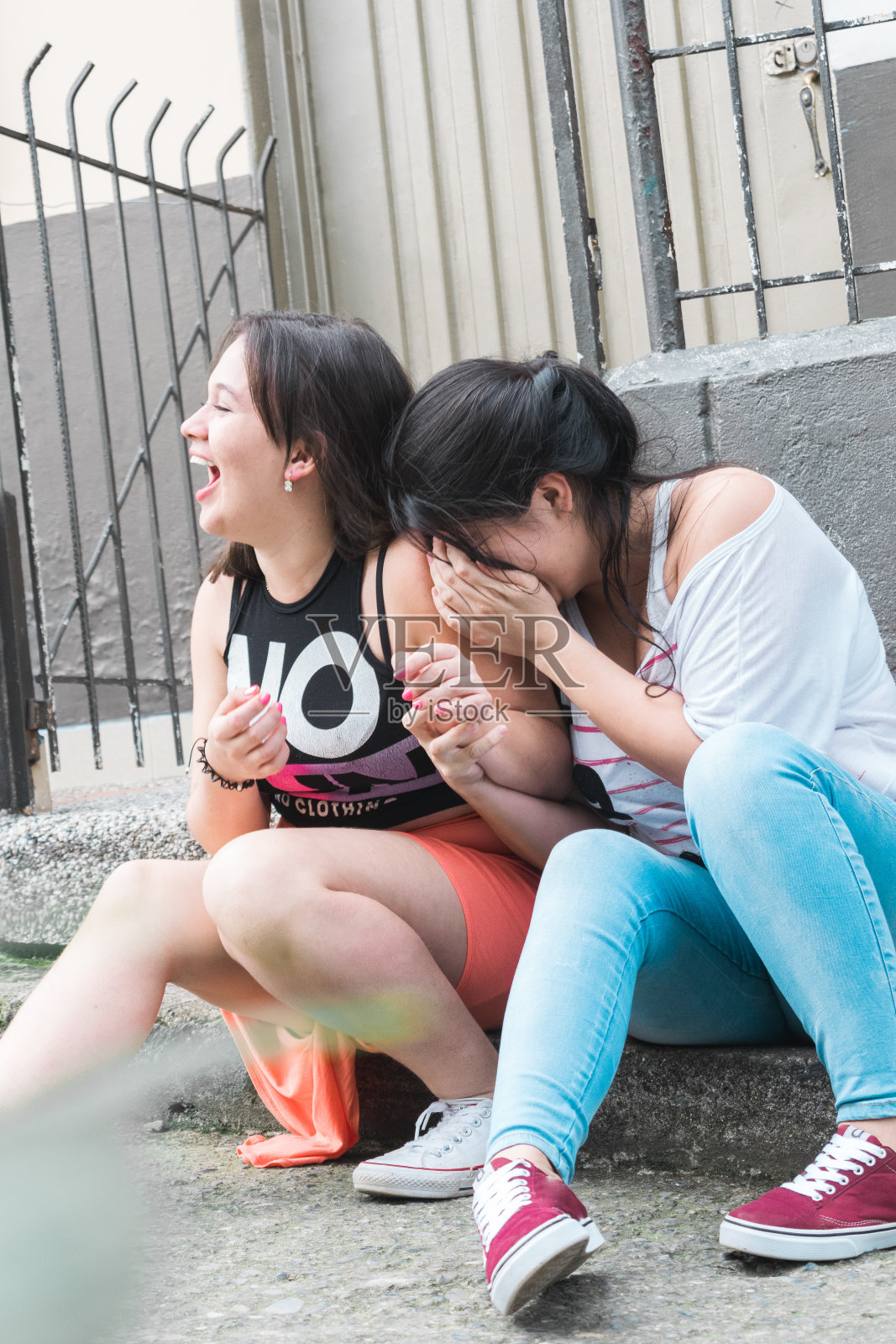 快乐的拉丁女孩开怀大笑，坐在城市户外的人行道上，友谊、忠诚、团结和爱情的概念。最好的朋友照片摄影图片