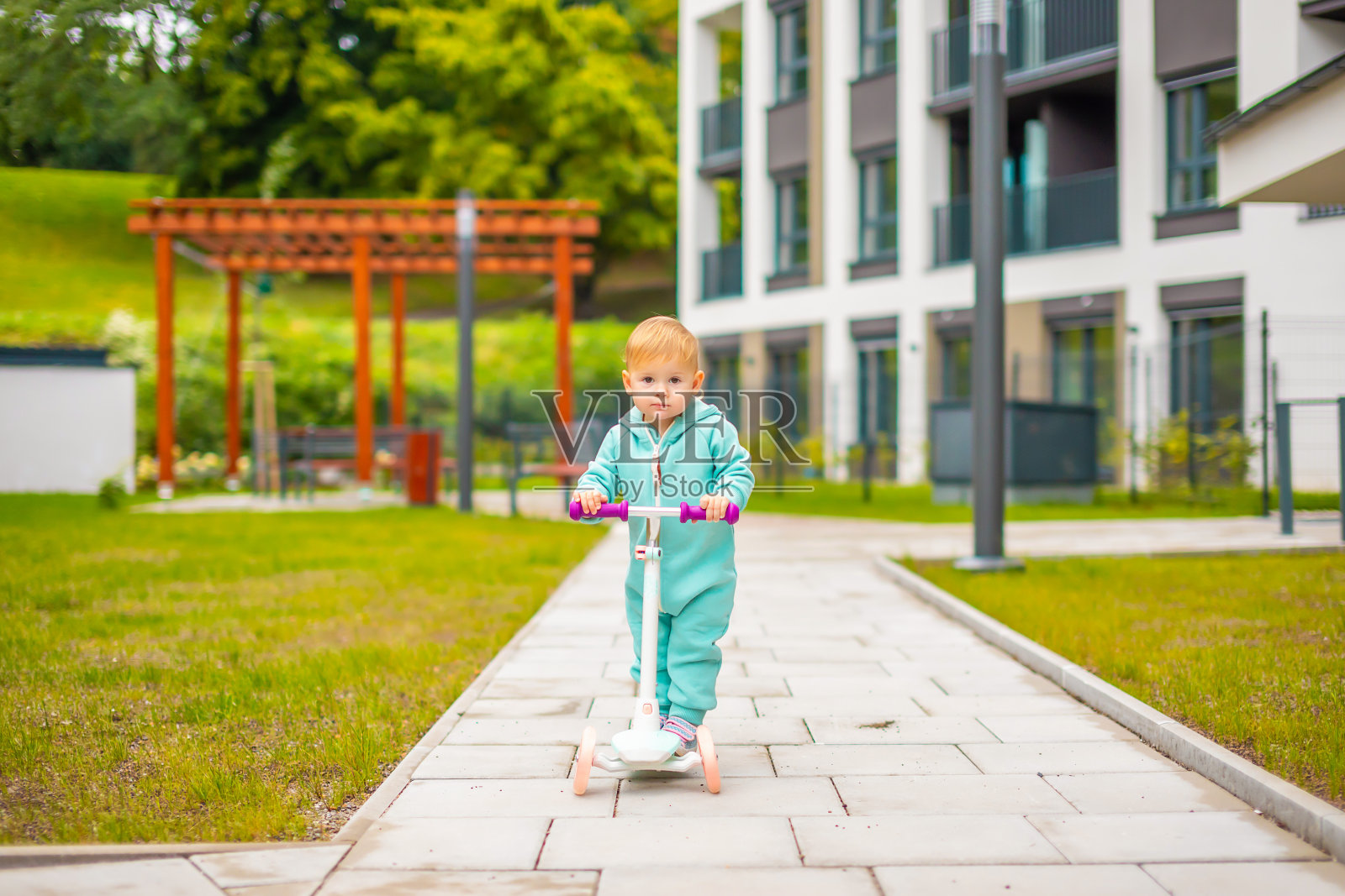 可爱的小女孩，穿着蓝色工装裤，骑着踏板车。快乐健康可爱的宝贝孩子在城市里玩得开心。孩子们在寒冷的户外活动。照片摄影图片