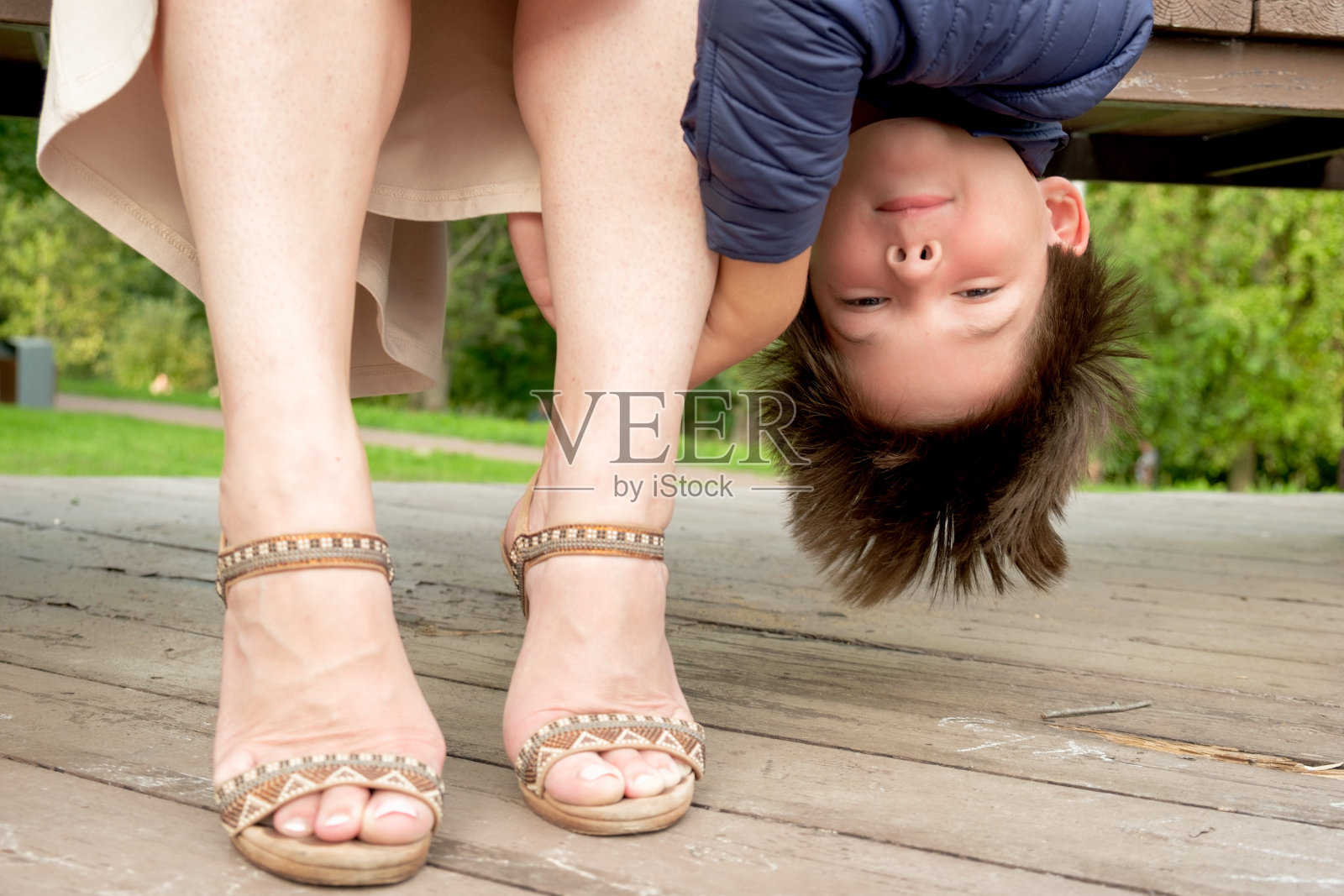 一个八岁的男孩倒挂在他妈妈的腿旁的长凳上照片摄影图片