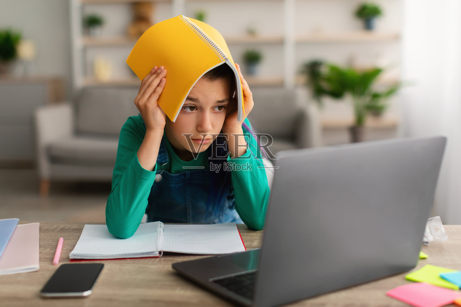 疲惫的小女孩，头上顶着笔记本照片摄影图片