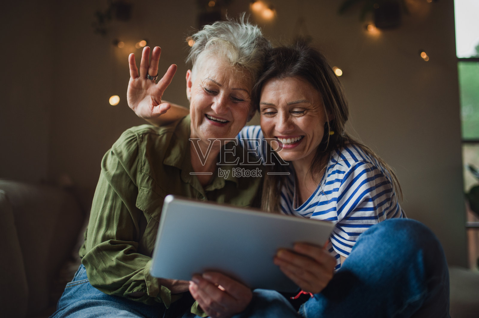 快乐的老年母亲肖像与成年女儿在家里使用平板电脑，视频通话的概念。照片摄影图片
