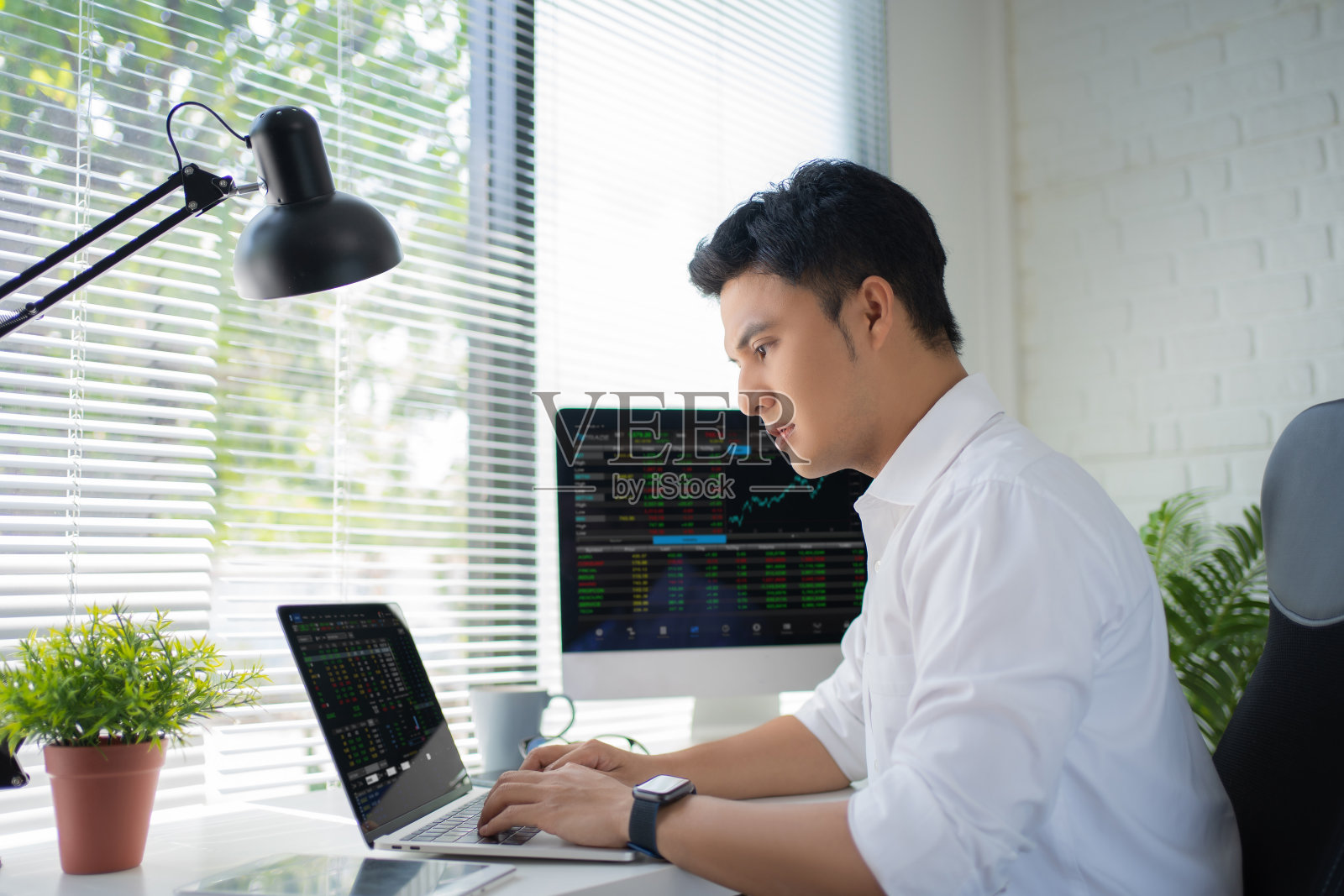 忙碌的亚洲年轻现代男人，穿着正装，坐在办公室里用电脑工作。照片摄影图片