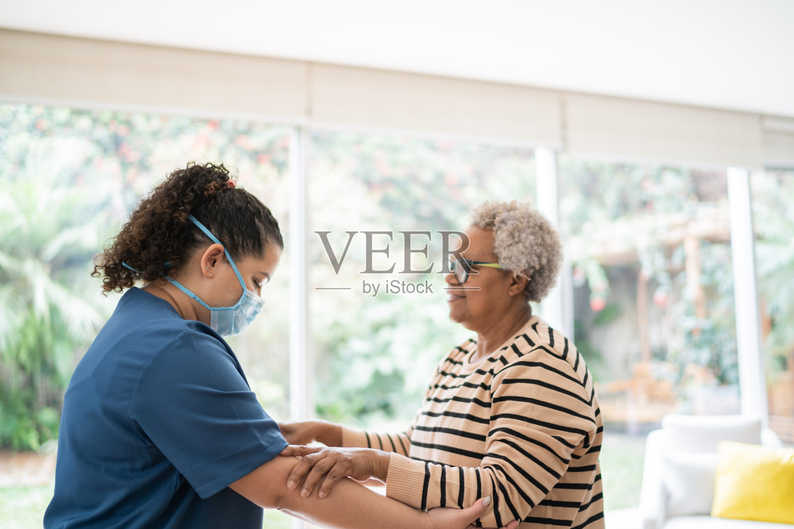 家庭护理员戴着防护口罩帮助老年妇女在家散步照片摄影图片