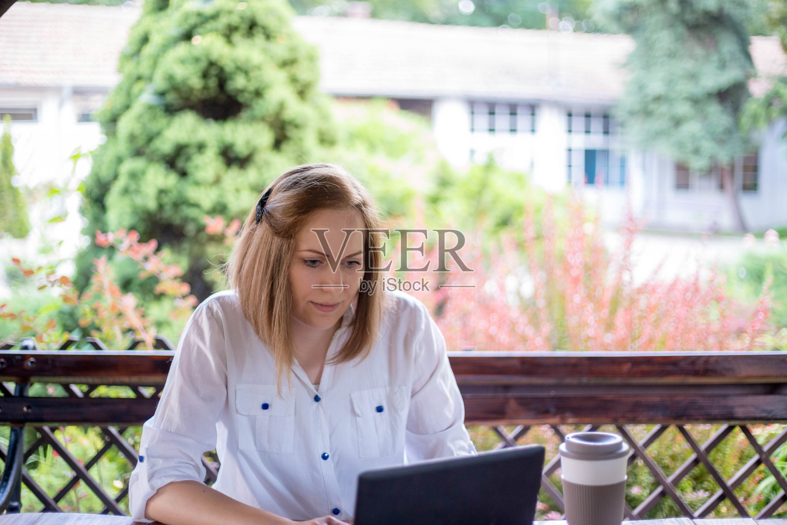 一位年轻的成年人坐在长椅上用笔记本电脑工作，她在公园的户外工作照片摄影图片