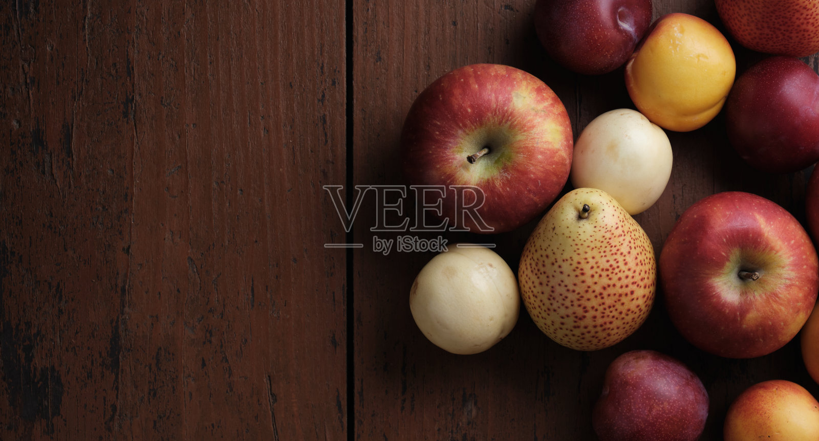 旧木桌上放着水果。苹果，梨，李子，杏子在暗红色的背景上照片摄影图片
