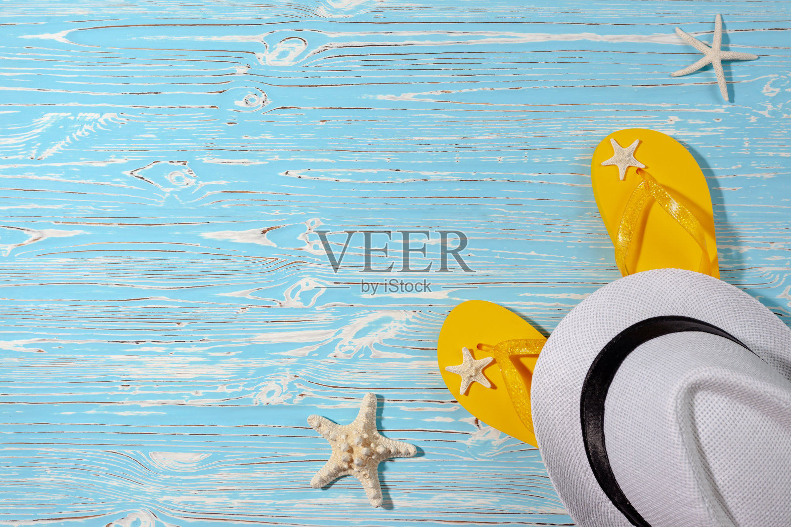 黄色橡胶人字拖，白色沙滩帽，蓝色木制背景上的海星照片摄影图片