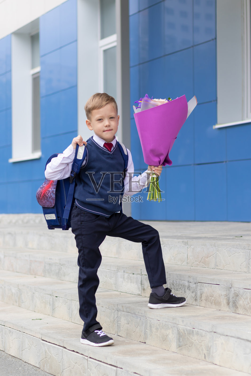9月1日假期结束后，一名可爱的一年级男孩穿着校服，手捧一束五颜六色的鲜花在校园里。知识的一天照片摄影图片