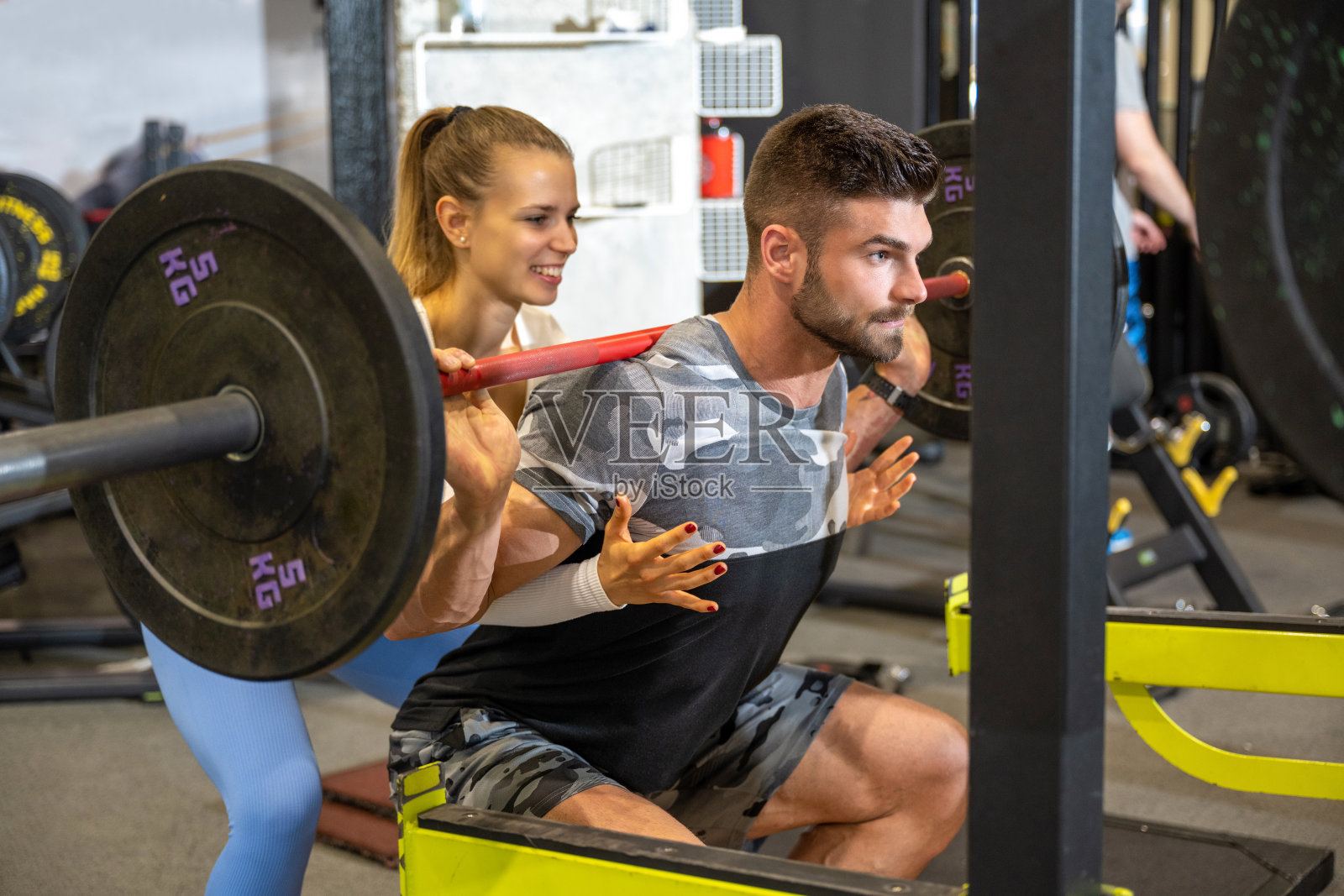 女性私人健身教练协助肌肉发达的男人与沉重的杠铃工作。运动，健身，团队合作，举重和人的概念。照片摄影图片