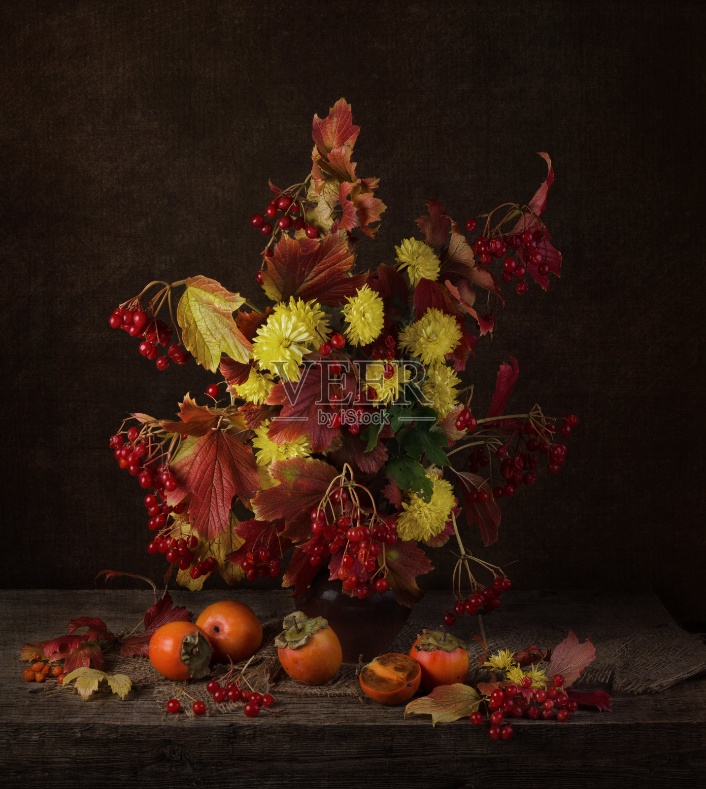 明亮的秋天静物与黄色的花朵和红色的荚莲浆果酒香在黑暗的背景照片摄影图片