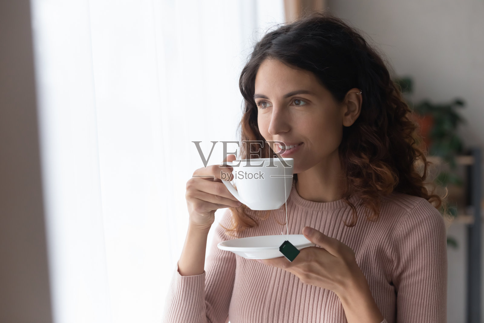 微笑的女人站在室内，端着一杯茶照片摄影图片