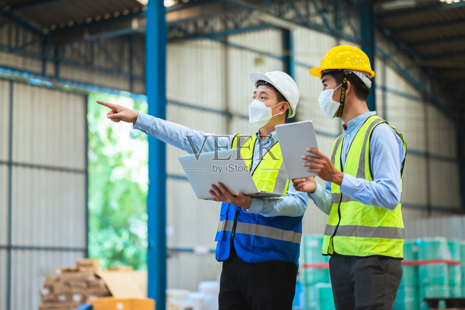 工程师和工头戴口罩、安全帽和背心。与口罩厂通过数据文件咨询讨论工业生产管理。员工在幕后工作。照片摄影图片