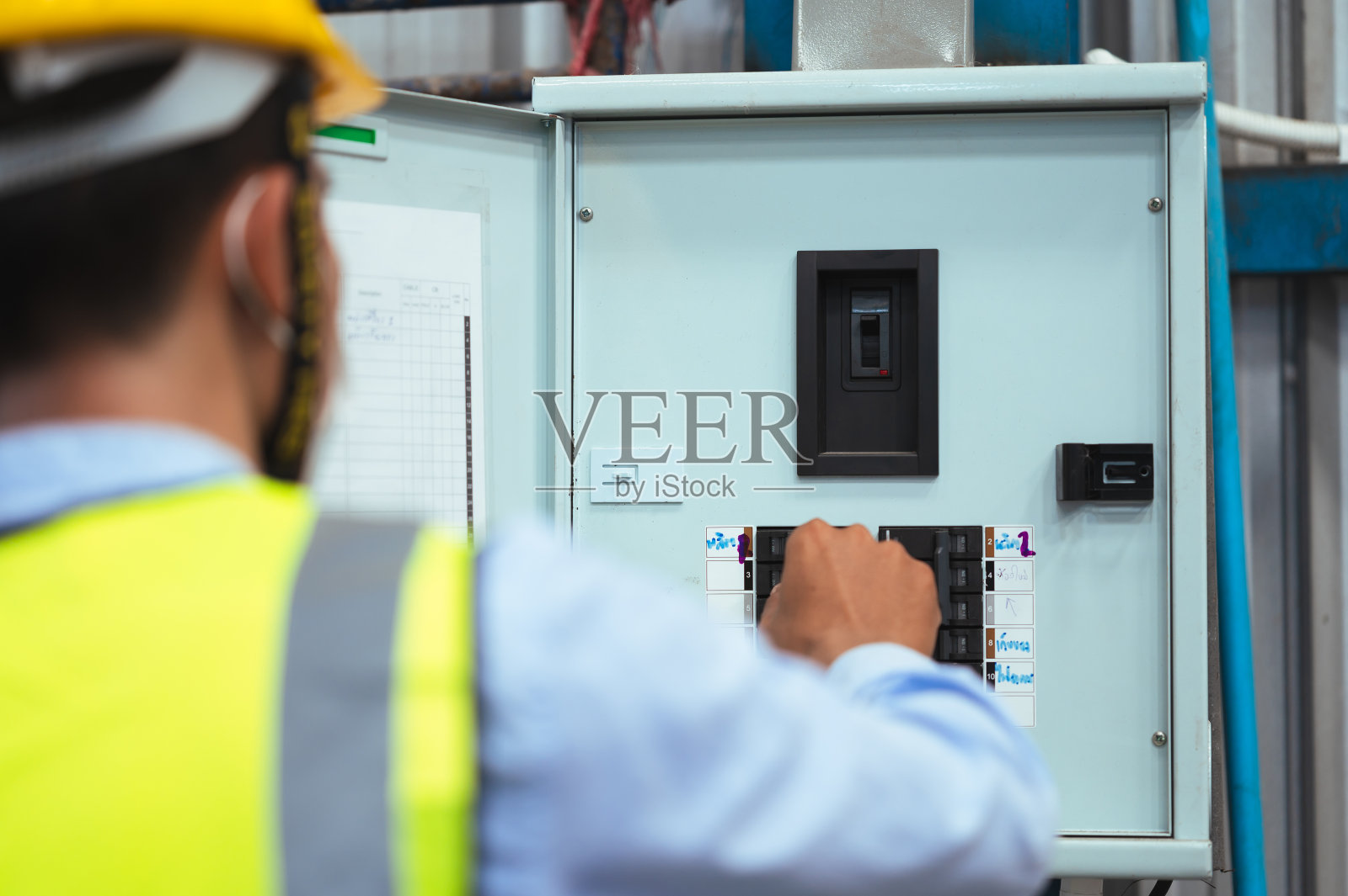 工程师，主管或工头男性，戴口罩，安全帽，穿背心。检查工厂内部的电源控制箱面板和电气系统。为了工作安全。照片摄影图片