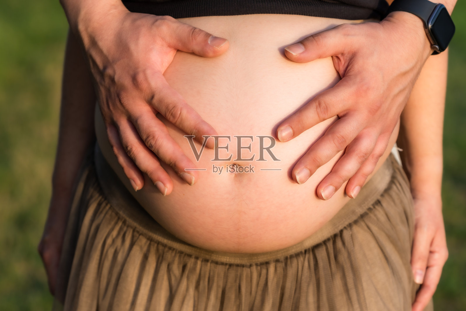 在户外，一个男人的手放在孕妇的肚子上照片摄影图片
