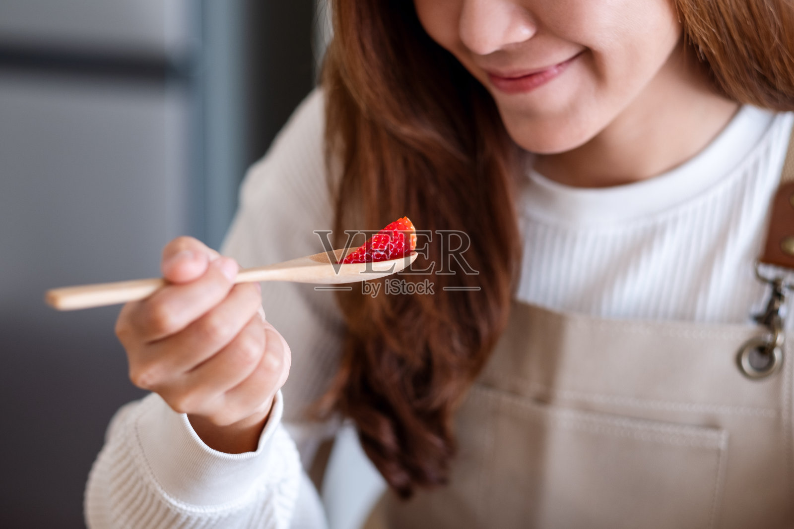 一个年轻的亚洲女人用勺子吃草莓照片摄影图片