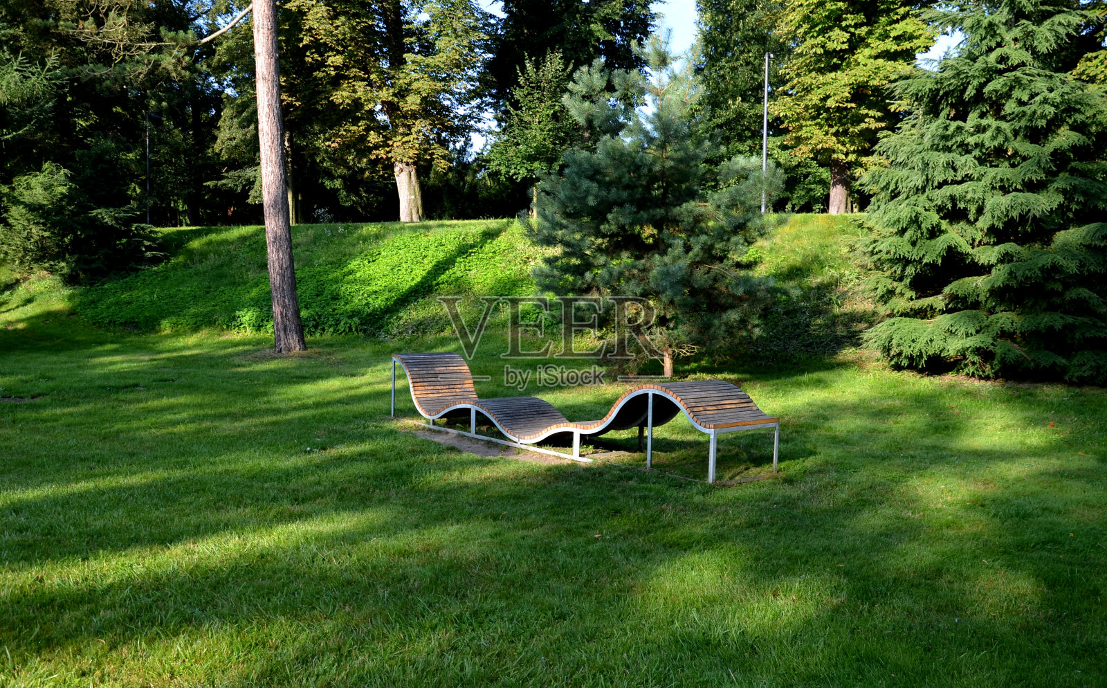 设计一个波浪线形状的长凳。金属镀锌框架上的木质镶板。这张长椅在城市公园里对年轻人来说是不常见的，坐着和躺着都很不寻常照片摄影图片