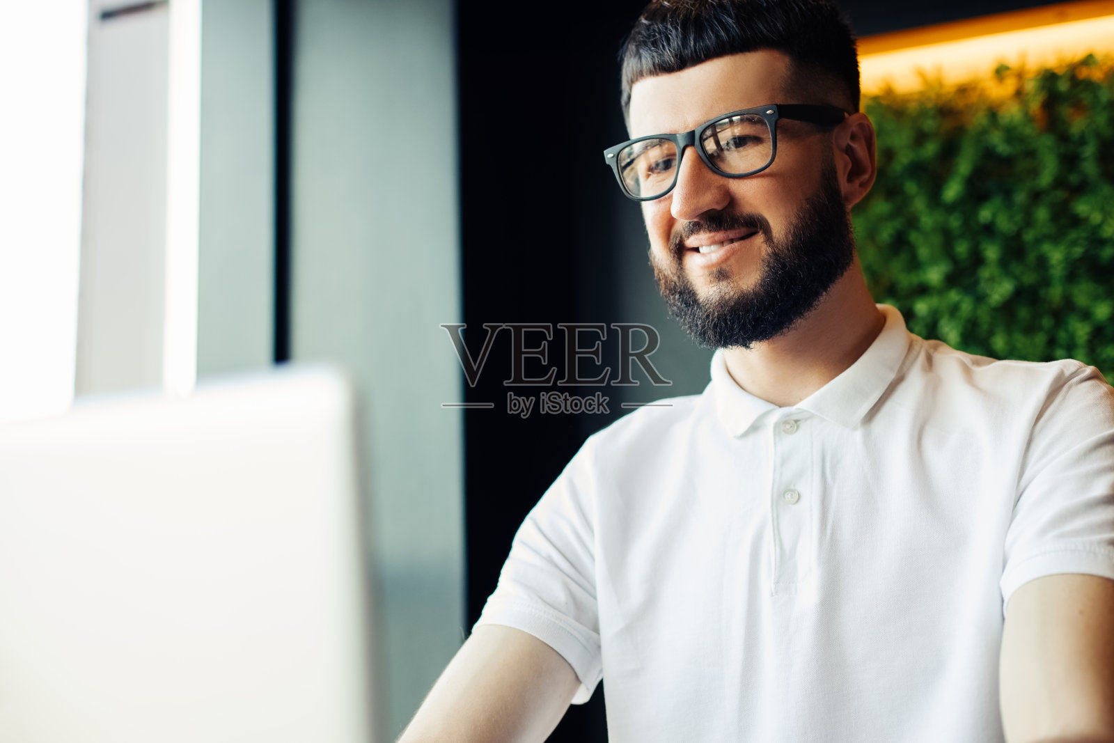 戴着眼镜，满脸胡须的年轻男子坐在咖啡馆的木桌旁，正在用笔记本电脑照片摄影图片