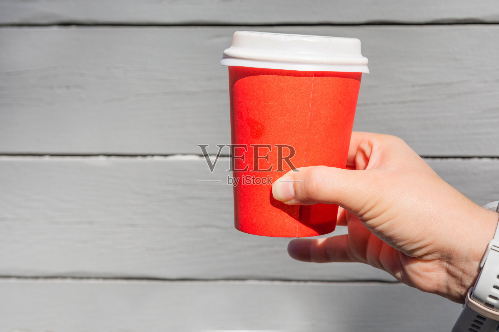 一位女性手拿着一个红色的纸制咖啡杯，背景是灰色的木头照片摄影图片