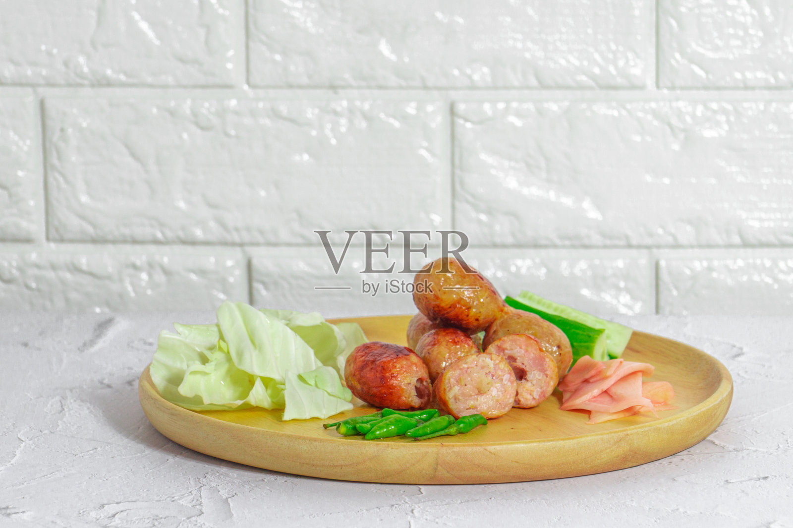 伊桑香肠是泰国著名的菜肴之一，伊桑香肠被盛在木制的盘子里，放在白色的桌子上，与辣椒和蔬菜一起吃。照片摄影图片