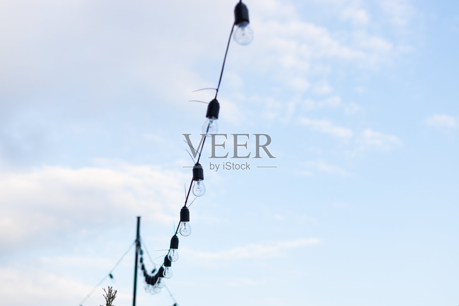 以蓝天为背景的灯具系列。街上的电子花环映衬着天空。用于照明的一排路灯照片摄影图片