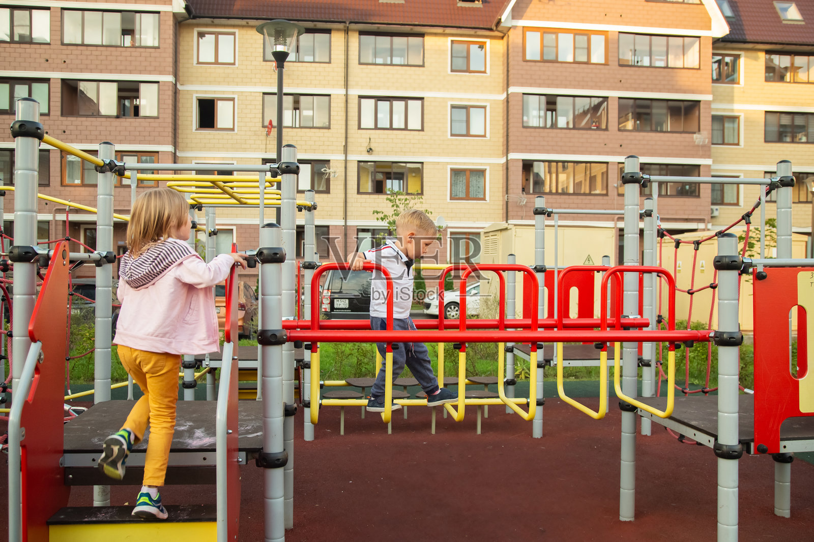 一个白人男孩和一个女孩在操场上爬，背景是房屋照片摄影图片