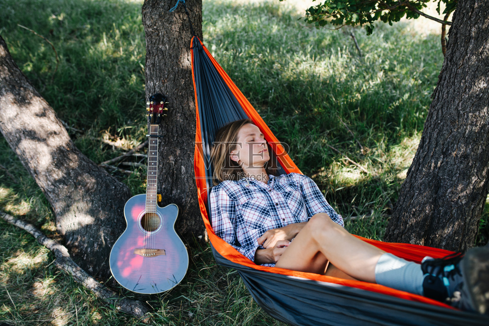 一个困倦的女人躺在吊床上，在两棵大树之间的阴影里。照片摄影图片
