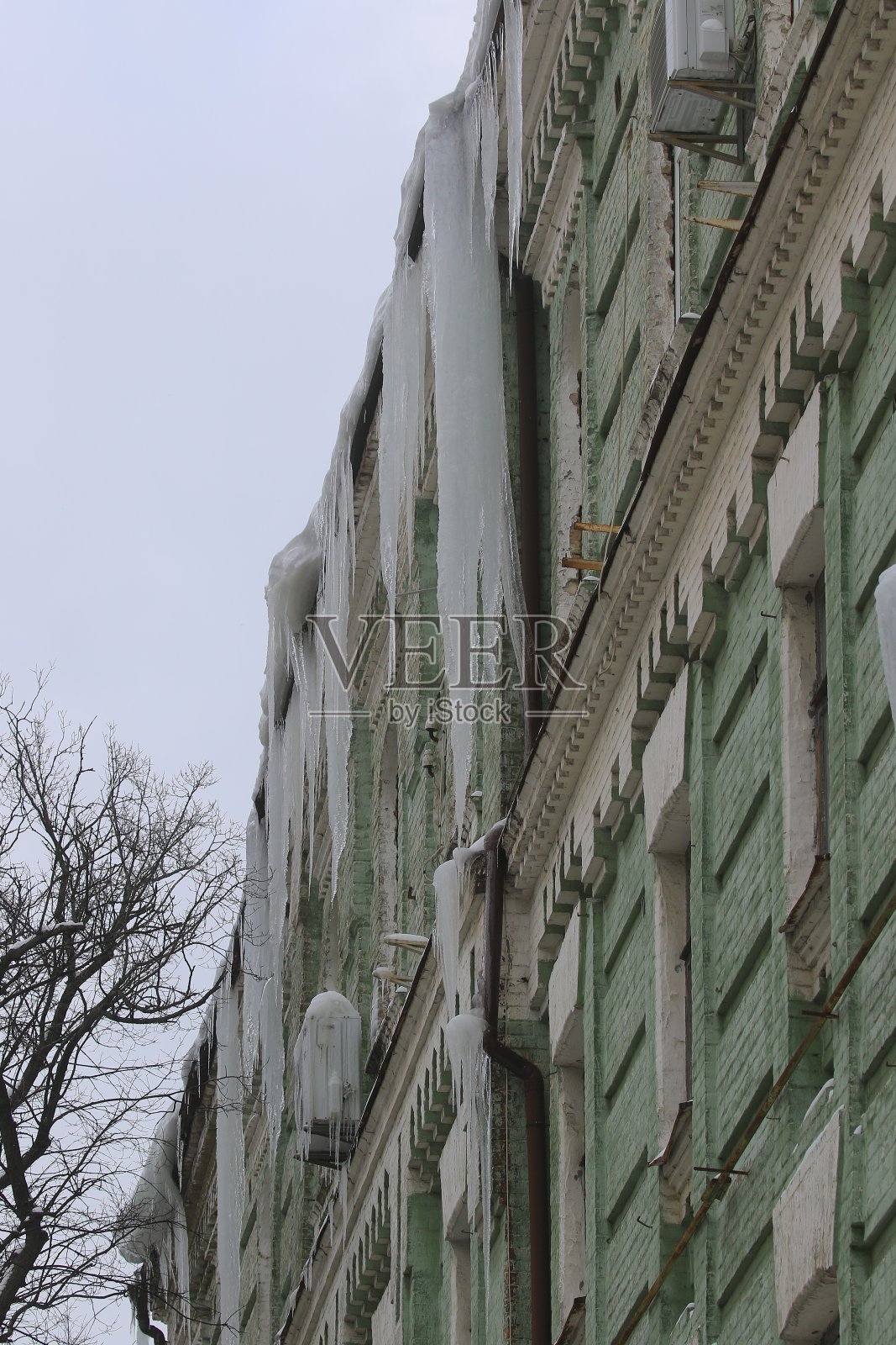 又大又尖的冰柱和融化的雪挂在屋顶的屋檐上。照片摄影图片