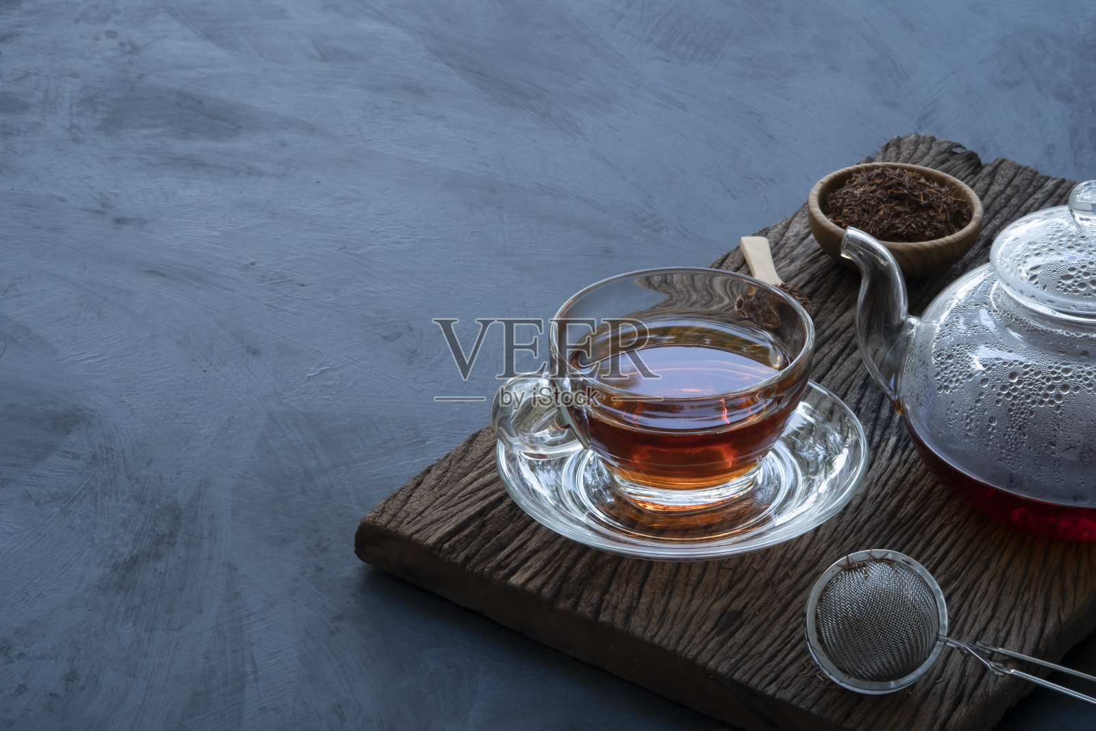 热茶装在玻璃茶壶里，杯子上装饰着干茶叶，小木碗和小勺子放在旧木板上，背景是深色的厨房桌子照片摄影图片