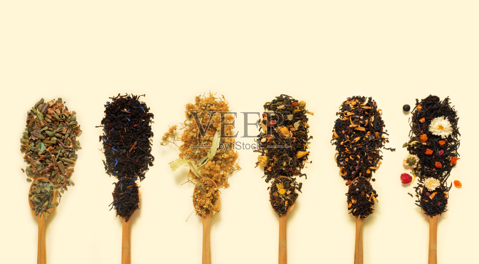 大品种的干茶在勺子从草药，鲜花，浆果和水果在黄色的纸背景。照片摄影图片