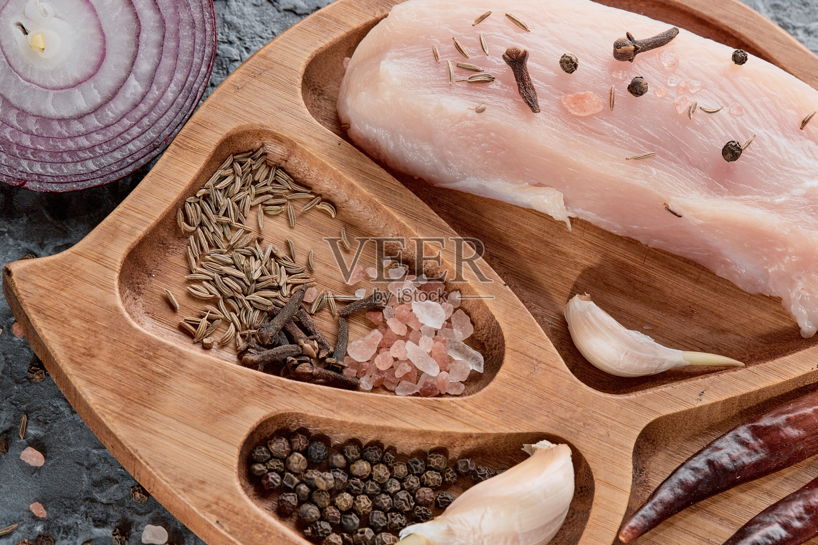 一个木碗里放着香料和新鲜的生鸡柳，背景是灰色的，旁边放着海盐、胡椒豌豆和大蒜。俯视图，复制空间，平铺照片摄影图片
