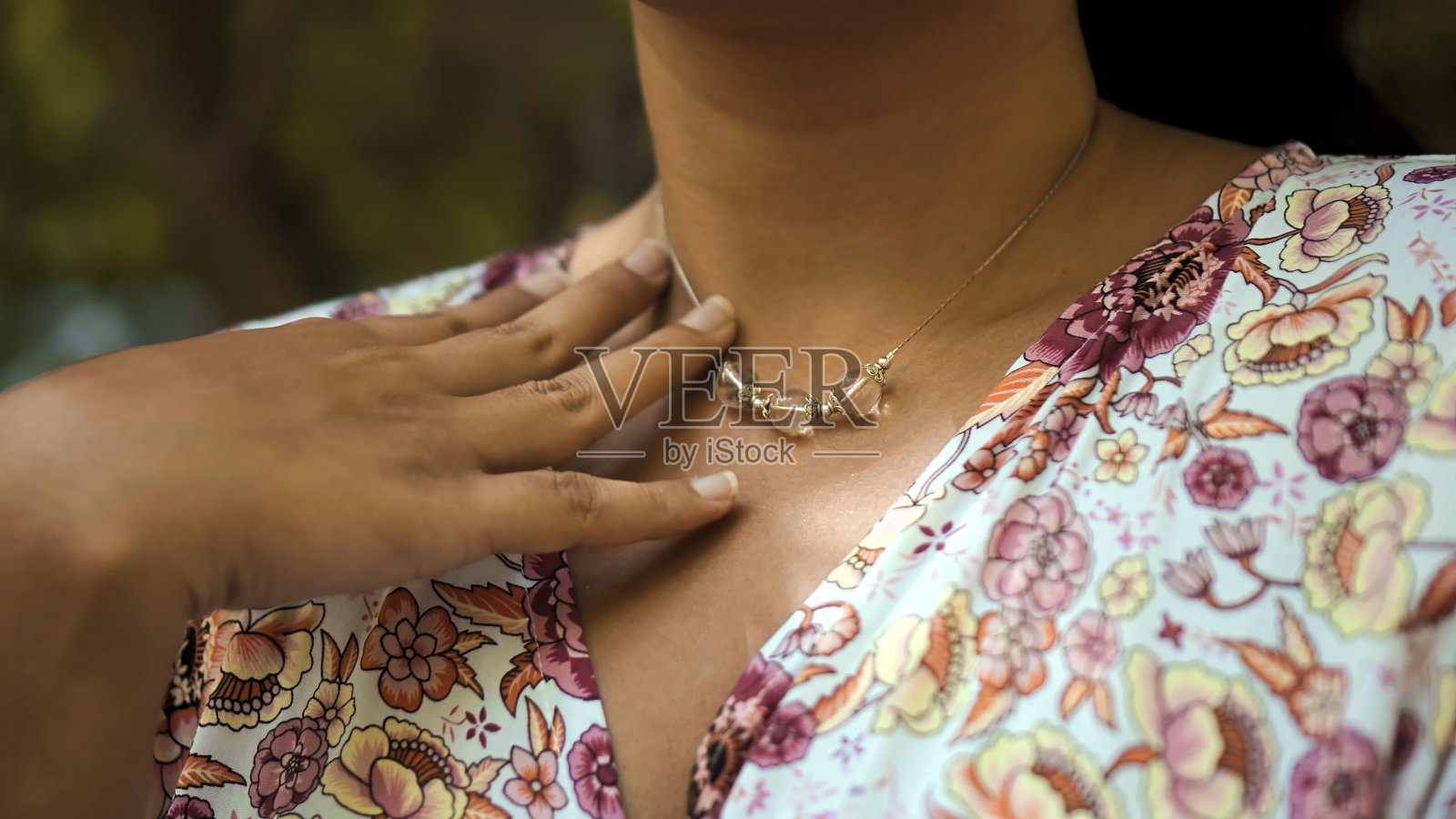 站在后院的黑发女孩，身着长裙，用手轻轻抚摸着挂在她脖子上的吊坠照片摄影图片