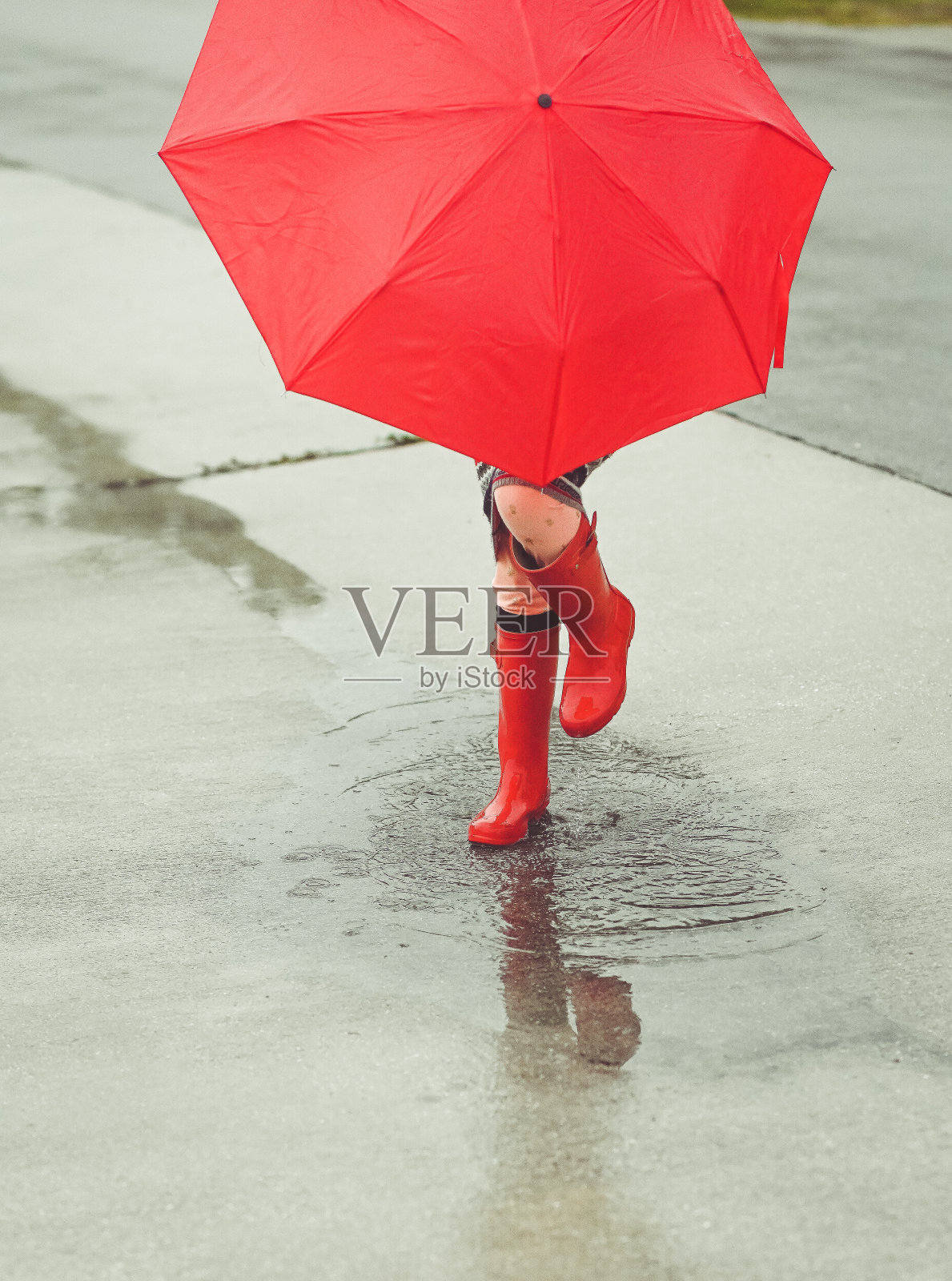 无名的孩子雨靴和伞在雨天的水坑里溅起水花照片摄影图片