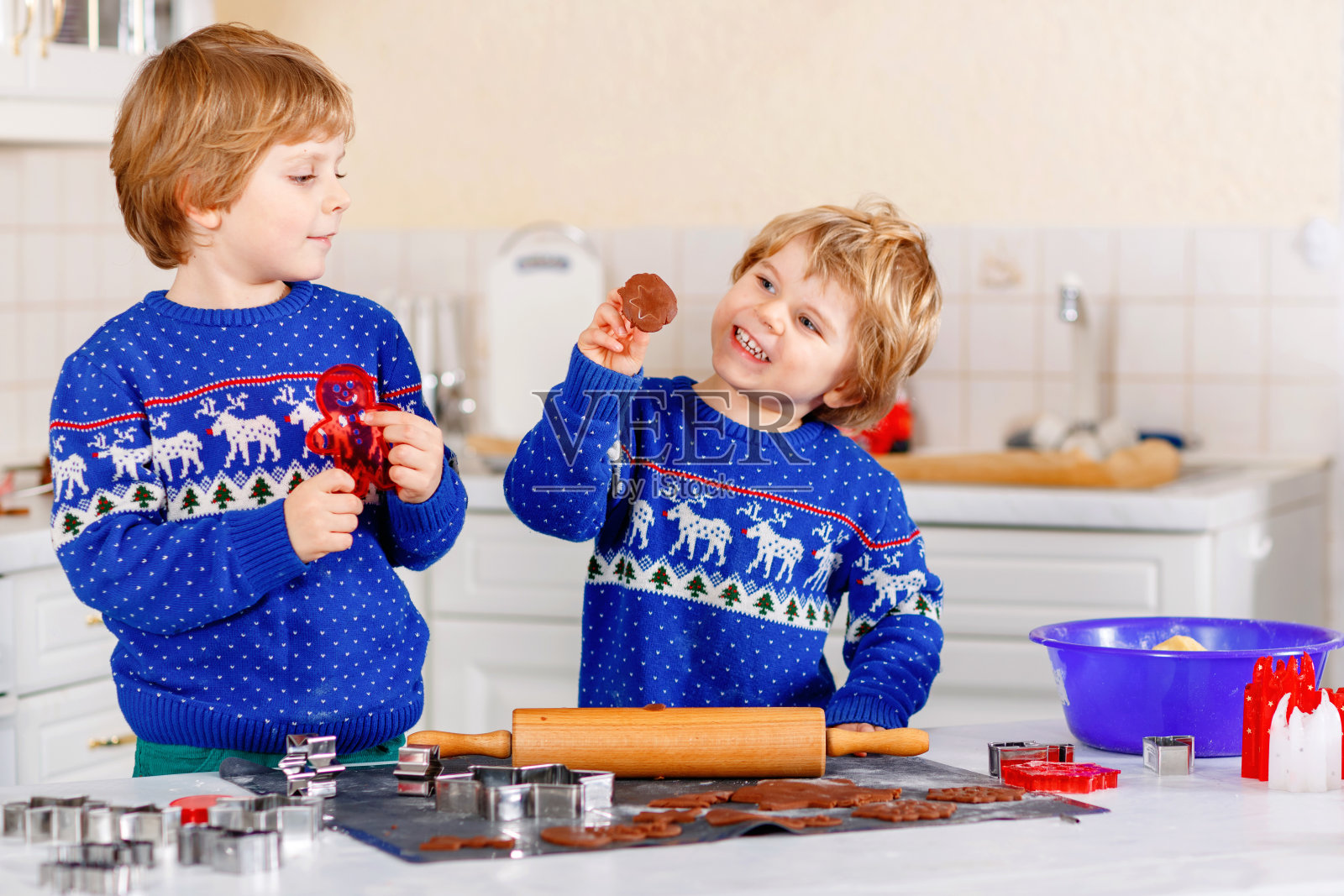 两个学前班的小男孩在烤姜饼。快乐的兄弟姐妹，穿着圣诞毛衣的孩子。厨房为圣诞节装饰。兄弟争斗，惹是生非。圣诞节的家庭活动照片摄影图片