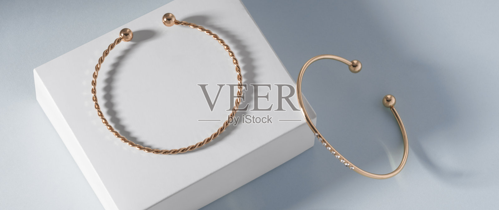 全景拍摄的两个现代金手镯上的白色盒子上的蓝色背景与复制空间照片摄影图片