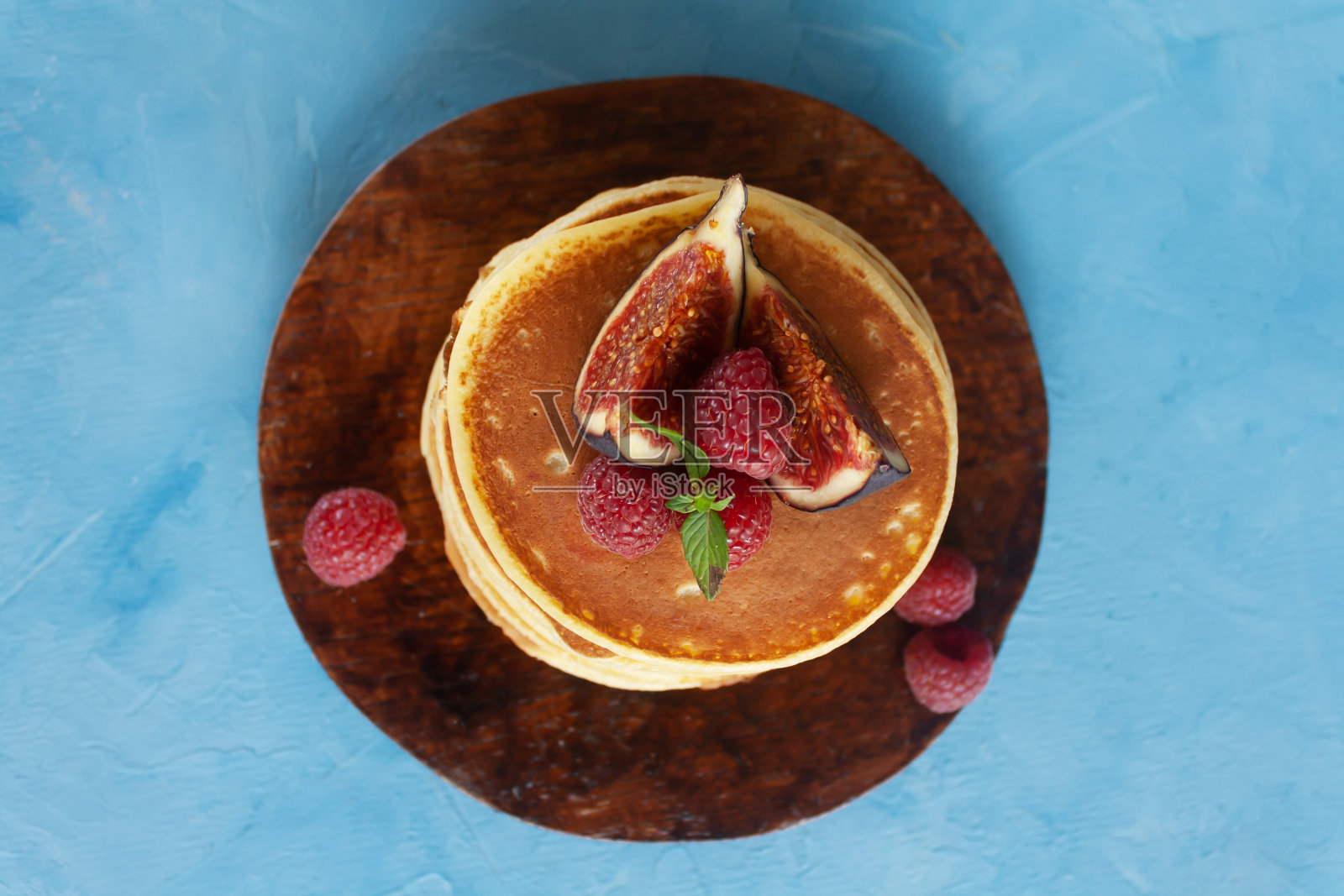 蓝色背景上有覆盆子和无花果的煎饼。照片摄影图片