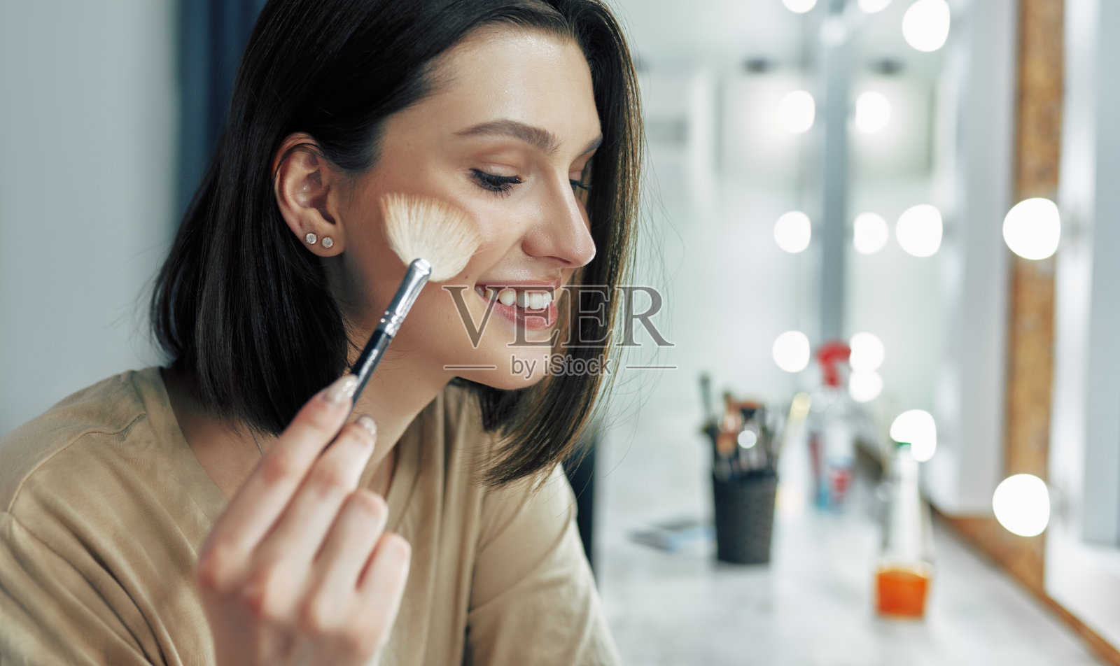 侧面的一个年轻的女人做一个在线教程，展示她最喜欢的有机美容产品。一个漂亮的女人一边看着镜头一边化妆。照片摄影图片