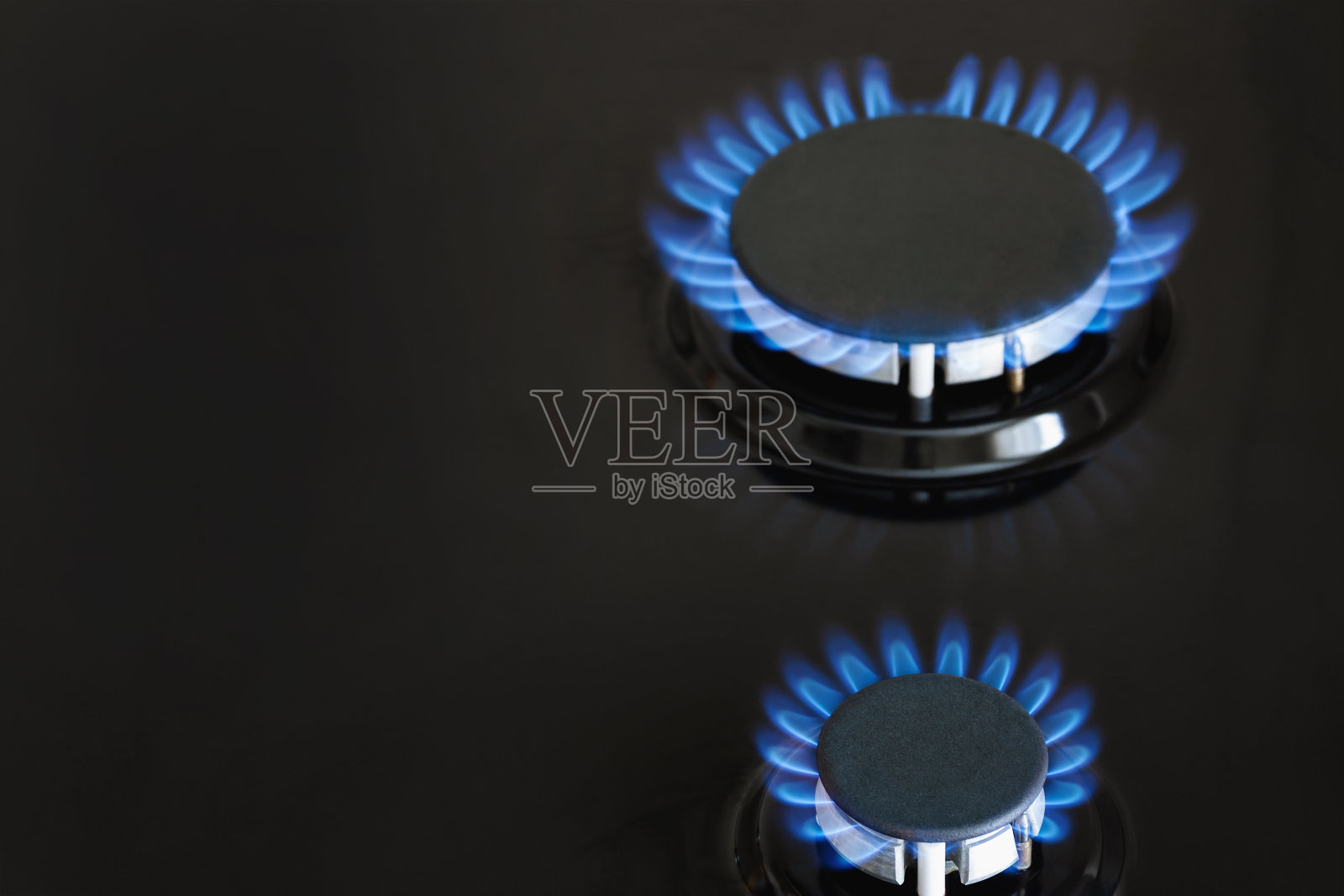 深色的炉子上，两个煤气炉在燃烧着蓝色的煤气灯。特写镜头,有选择性的重点照片摄影图片