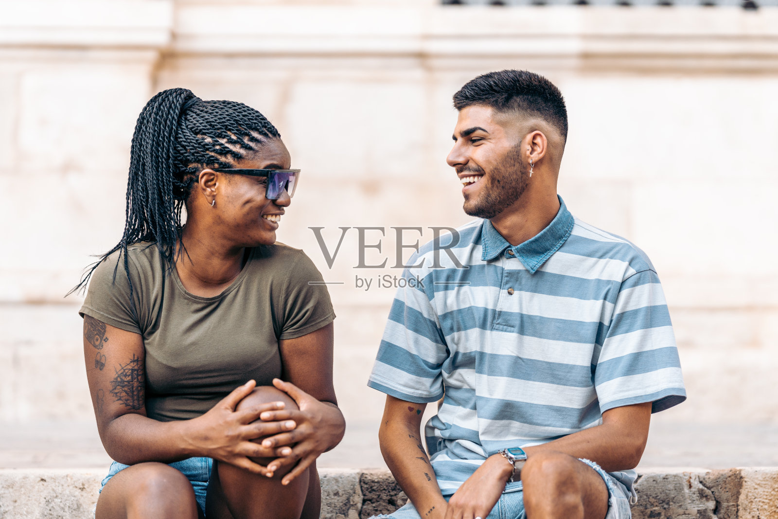 一个戴着墨镜纹身的黑人女人坐在一个在户外大笑的男人旁边照片摄影图片