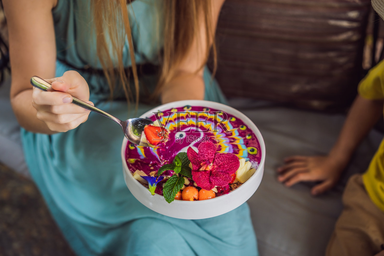 母亲和儿子坐在沙发上吃着地中海早餐，吃着健康的热带早餐，热带水果冰沙碗，装饰着五颜六色的姜黄和螺旋藻酸奶图案。它还装饰着水果和鲜花照片摄影图片